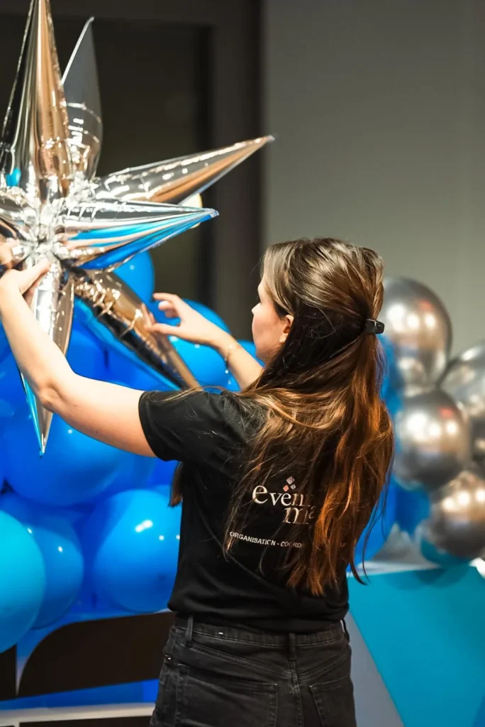 Christmas Party Asus - décoratrice fixant une étoile argentée sur une arche de ballons bleus par Event Machine