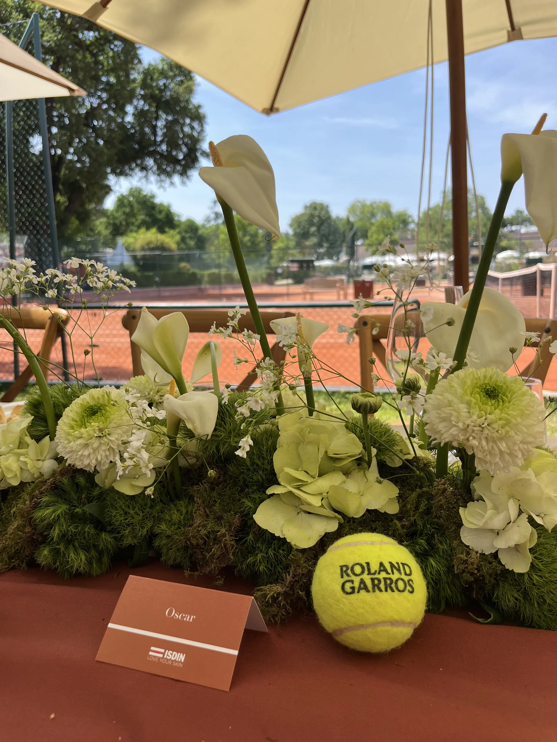 Déjeuner influenceurs ISDIN - balle Roland-Garros et marque-place au pied d'une composition florale, scénographie par Event Machine